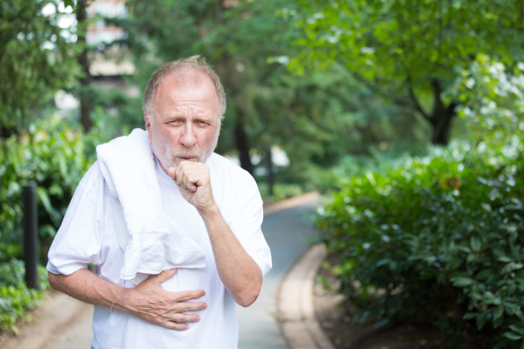 Older gentleman in white shirt with towel, coughing and holding stomach
