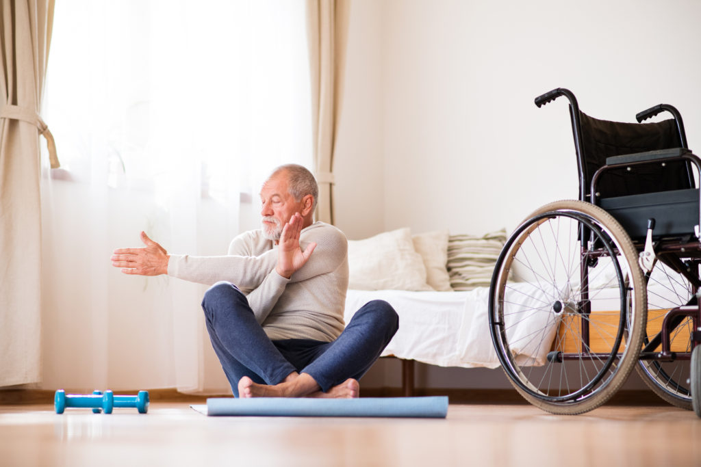 Active senior man doing exercise at home, with wheelchair by his side