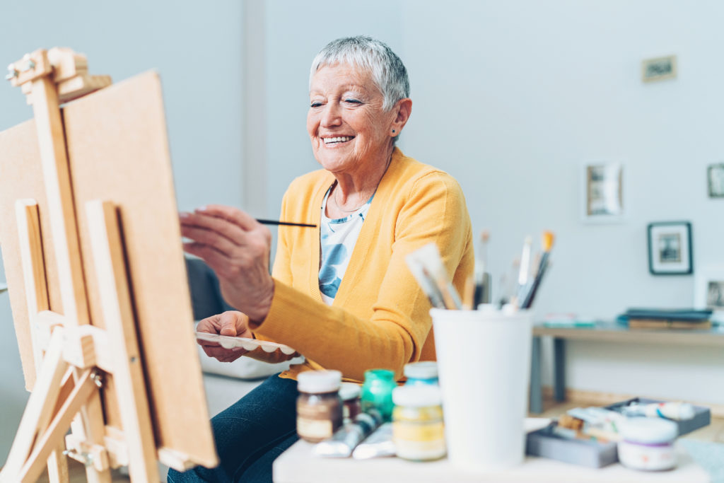 Senior woman sitting in front of easel, painting
