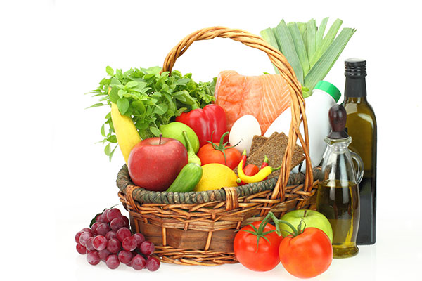 a basket of healthy foods, including salmon, eggs, tomatoes, apples, and olive oil