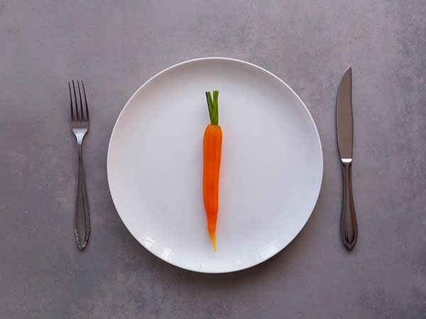 a lone carrot sitting on a white plate with a fork on one side and a knife on the other