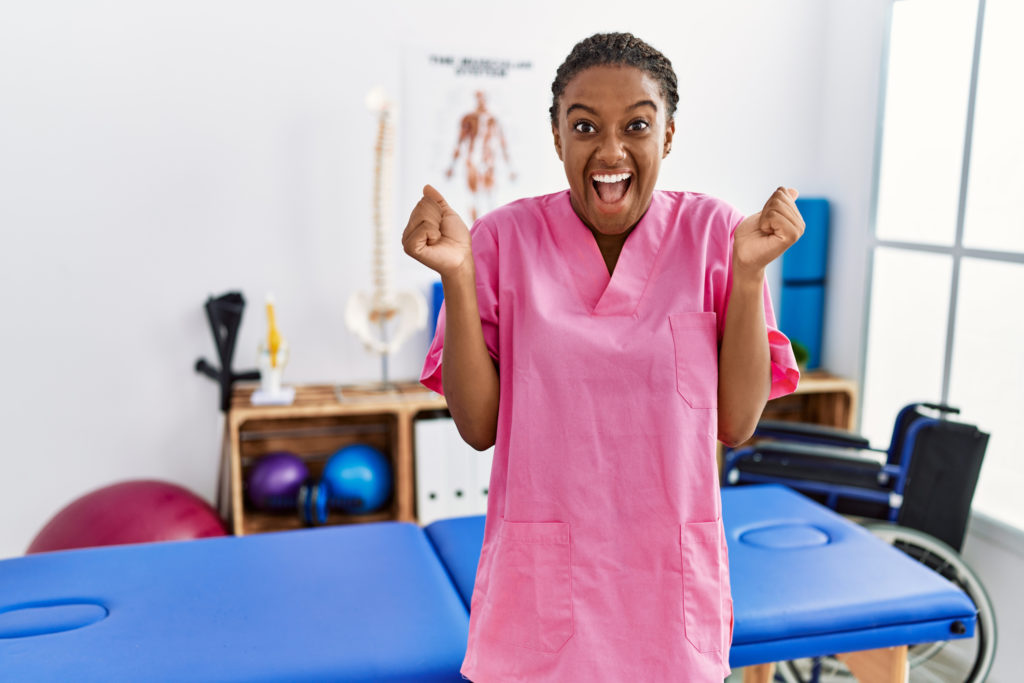 Young african american woman working at PT clinic celebrating surprised and amazed for success with arms raised and open eyes. winner concept.