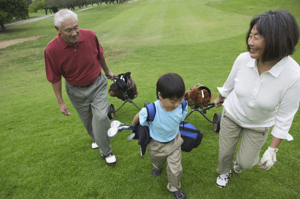 High angle view of an Asian gandparents and grandson walking on the green of a golf course.