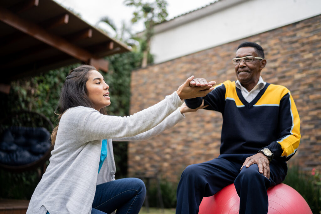 Black senior man doing exercise lifting arms with physical therapist outside.